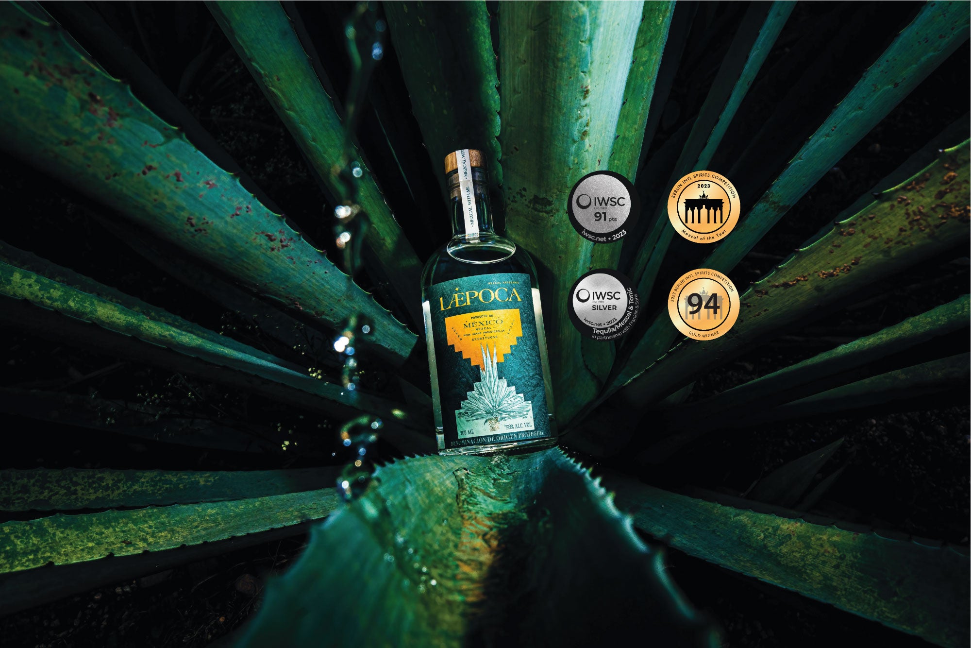 LÆPOCA Mezcal Flasche in der Mitte einer Agavenpflanze. Zudem sind vier Awards auf dem Bild zu sehen, die der Mezcal Laepoca gewonnen hat.